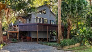 Une maison à deux étages dotée d’un balcon, entourée d’une végétation luxuriante.