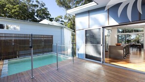 Een modern huis met een zwembad, grote glazen schuifdeuren en een houten terras.