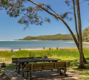 Een picknicktafel en bankjes aan een strand, met uitzicht op het water en heuvels in de verte.