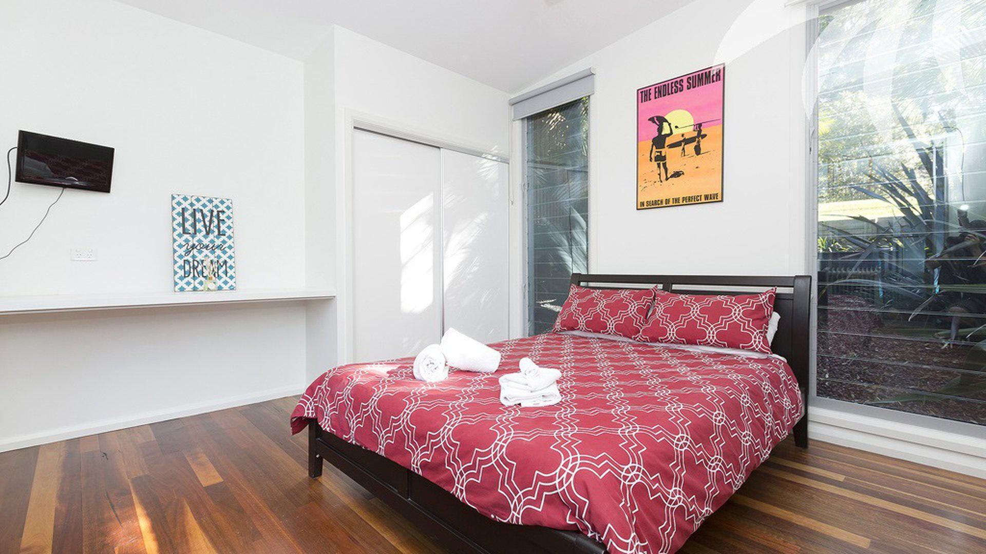 A bedroom with a bed, a TV, a poster, and a window.