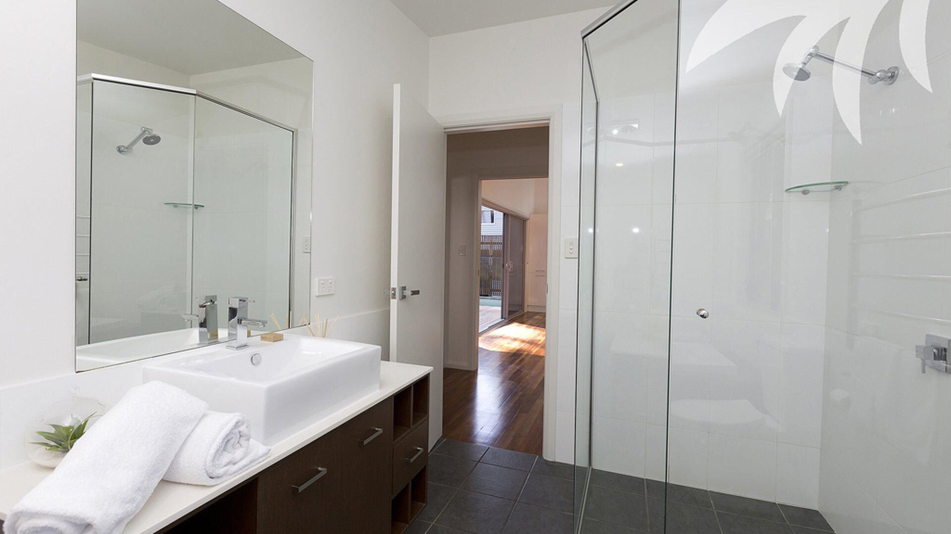 A modern bathroom with a glass shower enclosure, a large mirror, and a white sink.