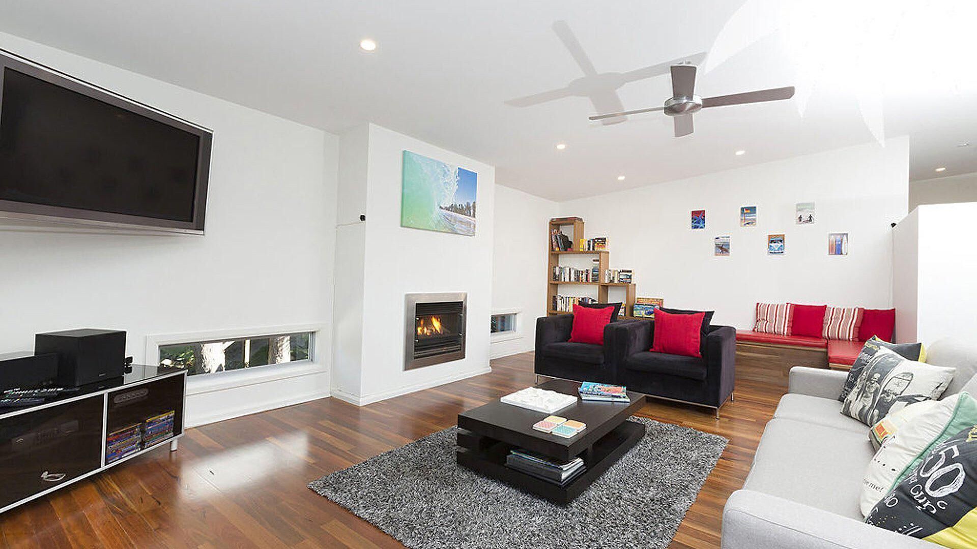 Una sala de estar moderna con chimenea, un televisor de pantalla plana, un sofá negro, un sofá blanco y un ventilador de techo.