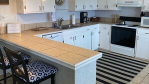 Una cocina moderna con armarios blancos, una isla central con taburetes altos, microondas, estufa e iluminación colgante.