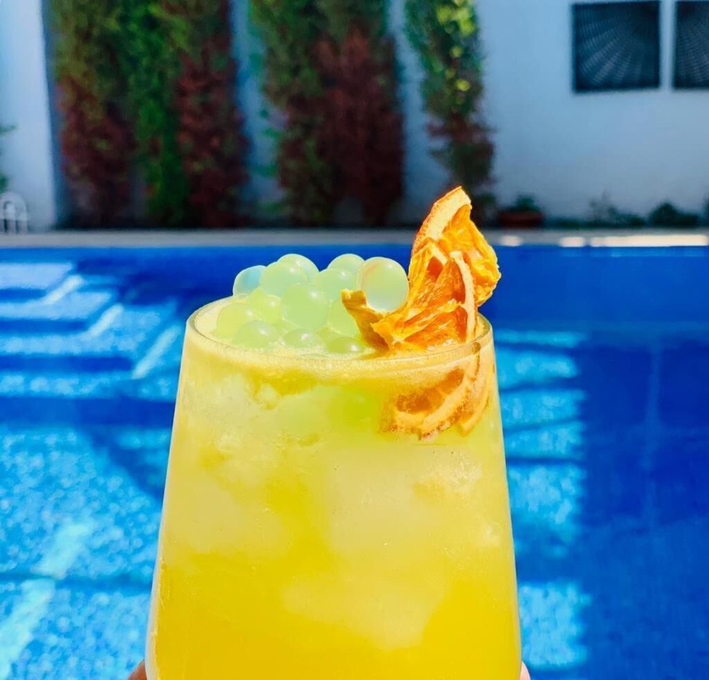 Un verre d’une boisson jaune, agrémentée d’une garniture, tenu devant une piscine.