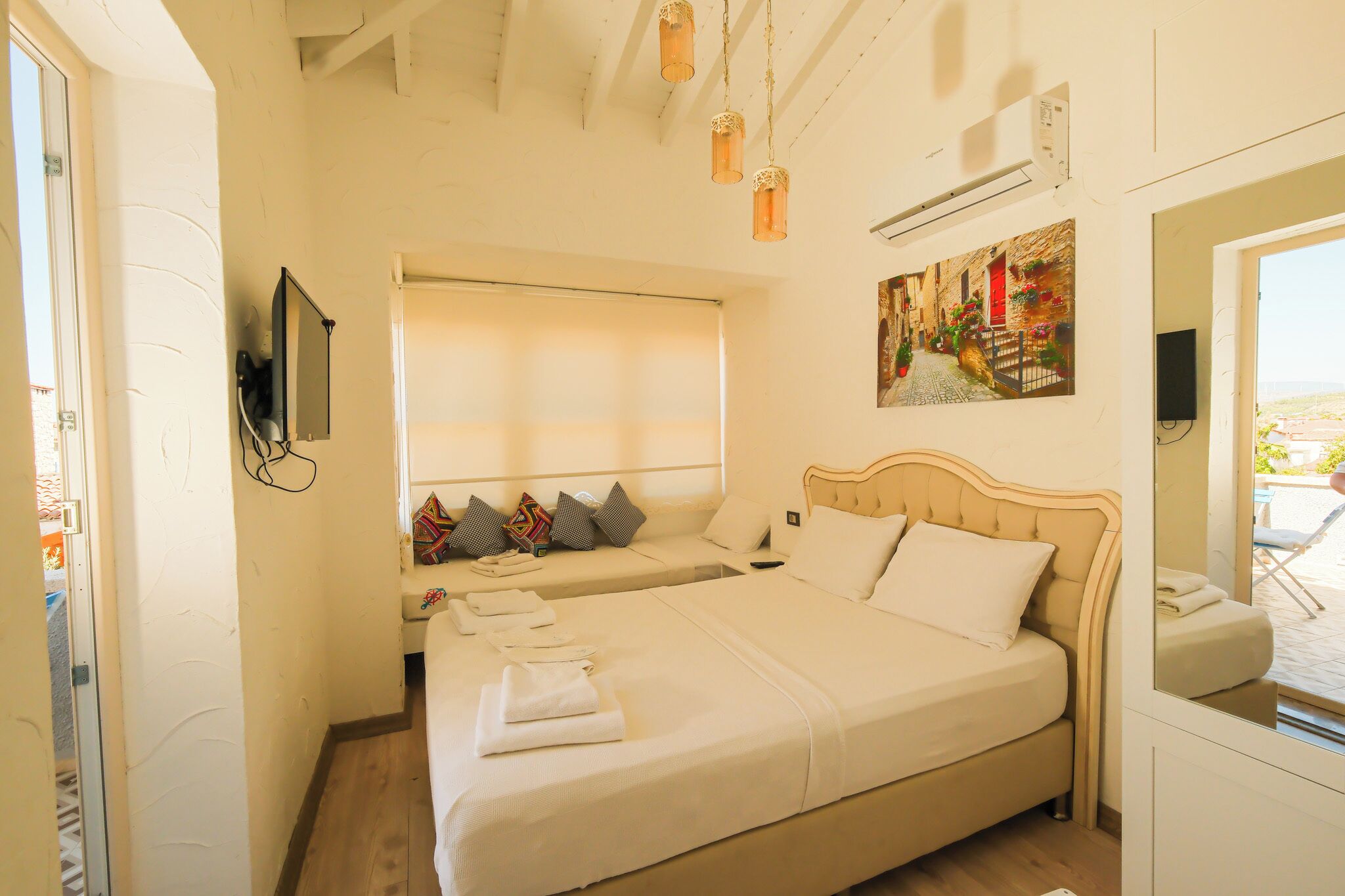 A hotel room with a large bed, a smaller bed, a window, a painting, and a TV on the wall.