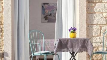 Un pequeño espacio al aire libre con mesa y sillas, una ventana con cortinas y una pared de piedra.