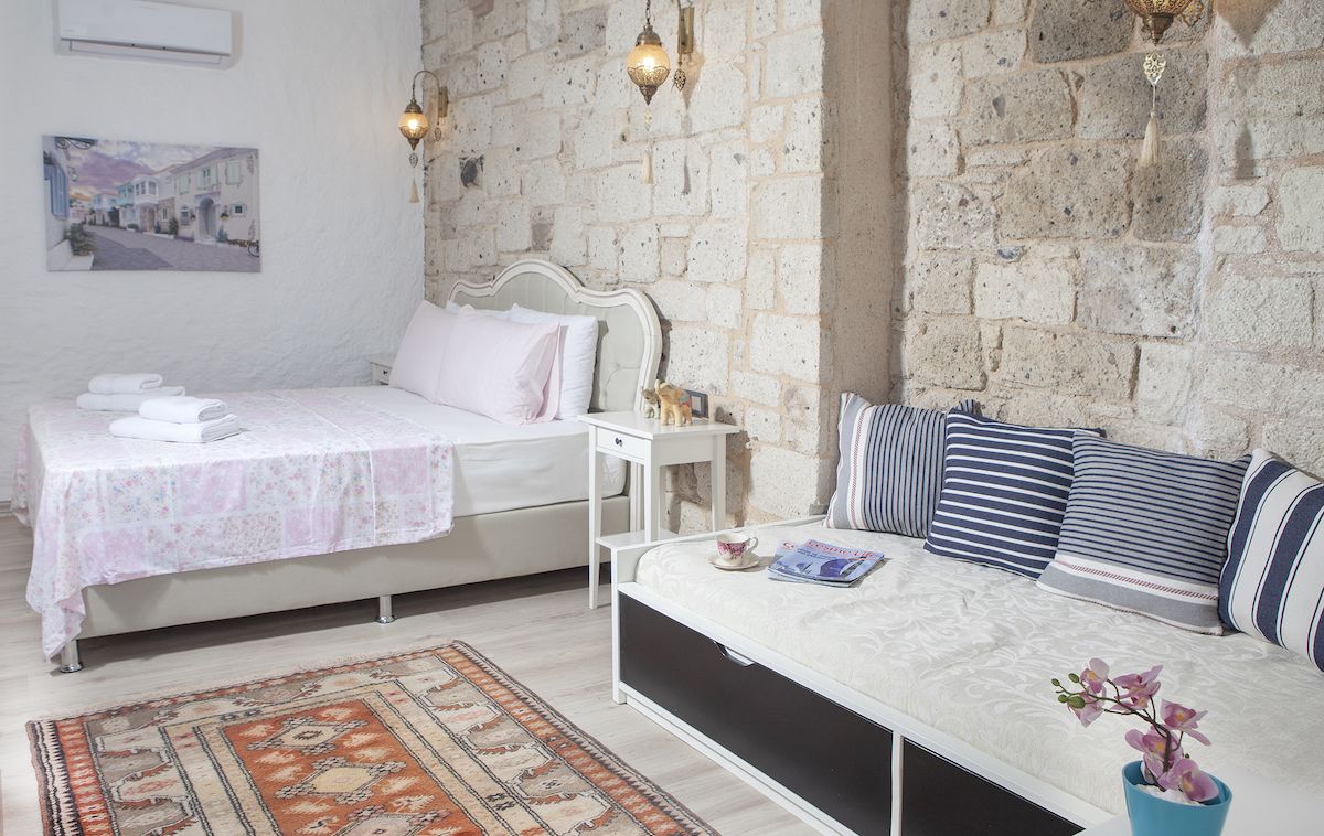 Un dormitorio con pared de piedra, una cama con almohadillas a rayas, una mesita de noche con lámpara y una planta pequeña.