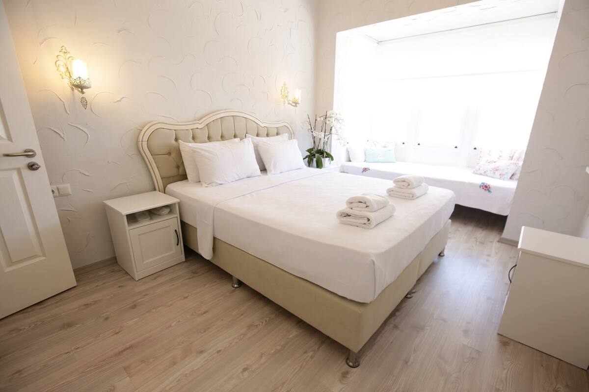 Een slaapkamer met een groot bed, nachtkastjes, een klein bureau en een raam met uitzicht.