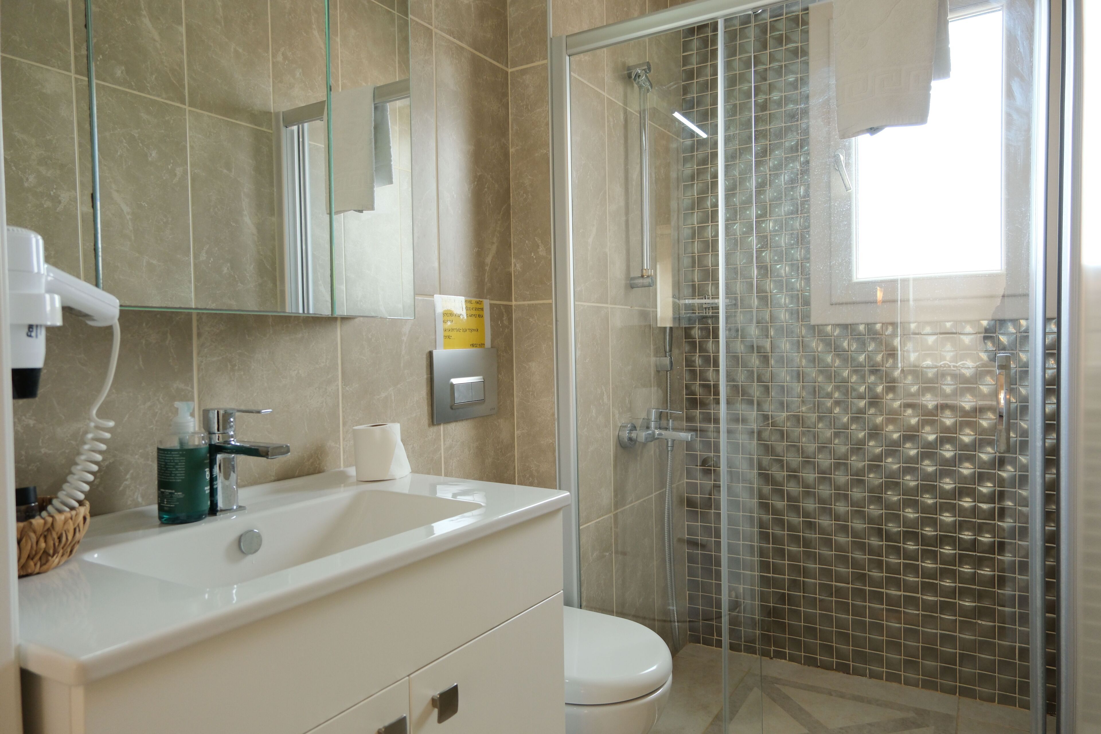 A bathroom with a white sink, mirror, and toilet. There is a shower area with a glass door and tiled walls.