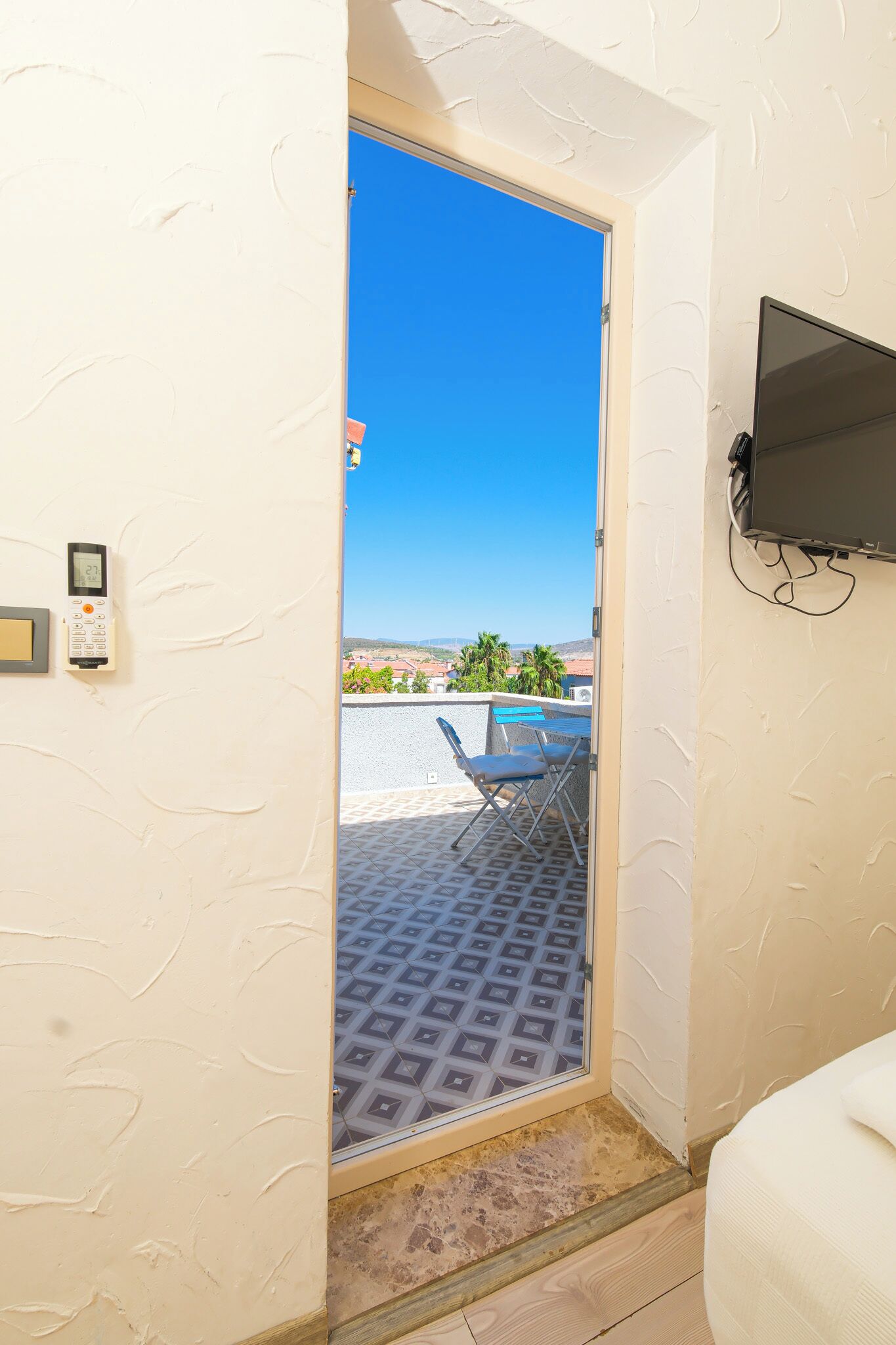 A room with a door leading to an outdoor area with a view of palm trees and a tiled floor.