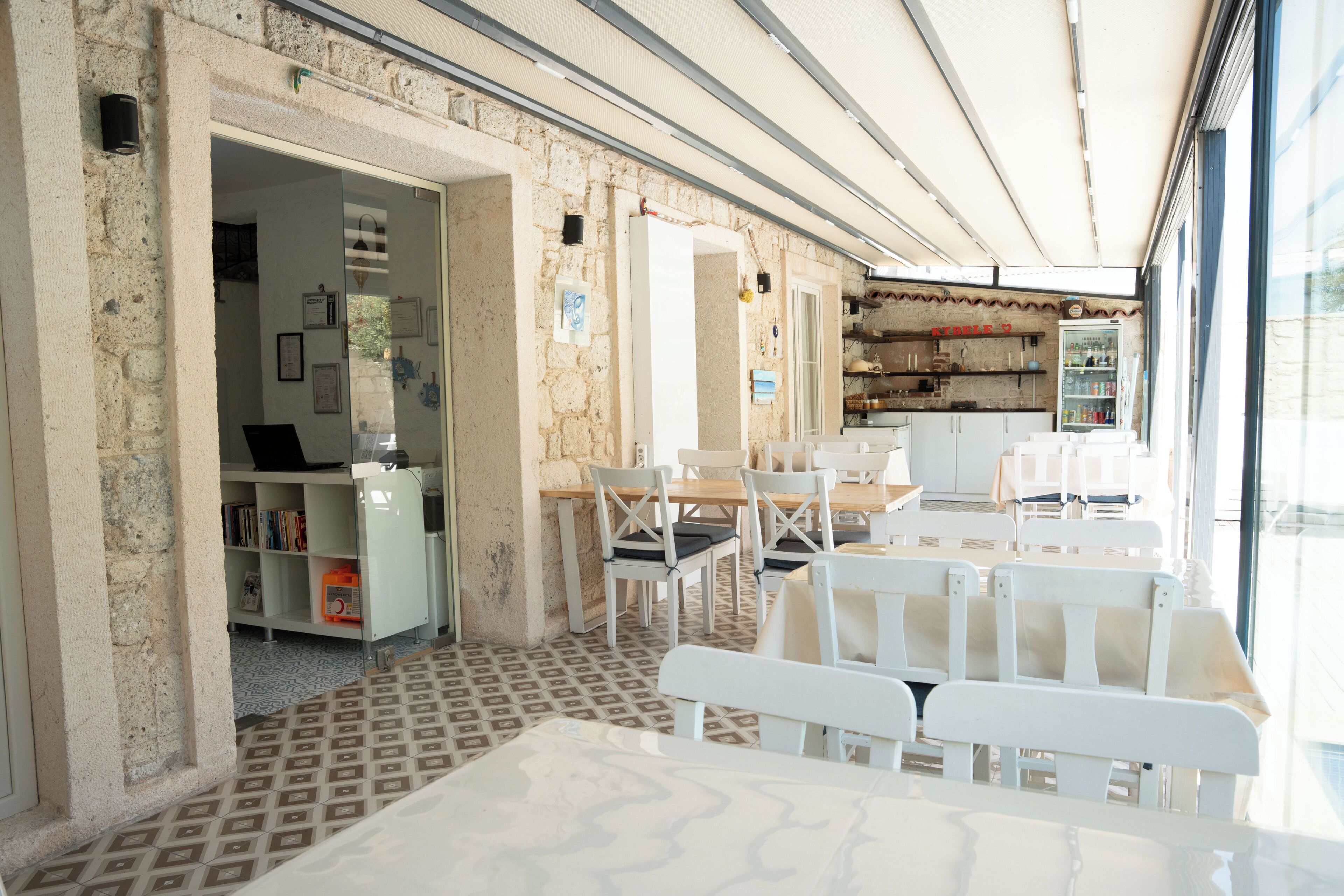A cafe with white furniture, a tiled floor, and a stone wall.
