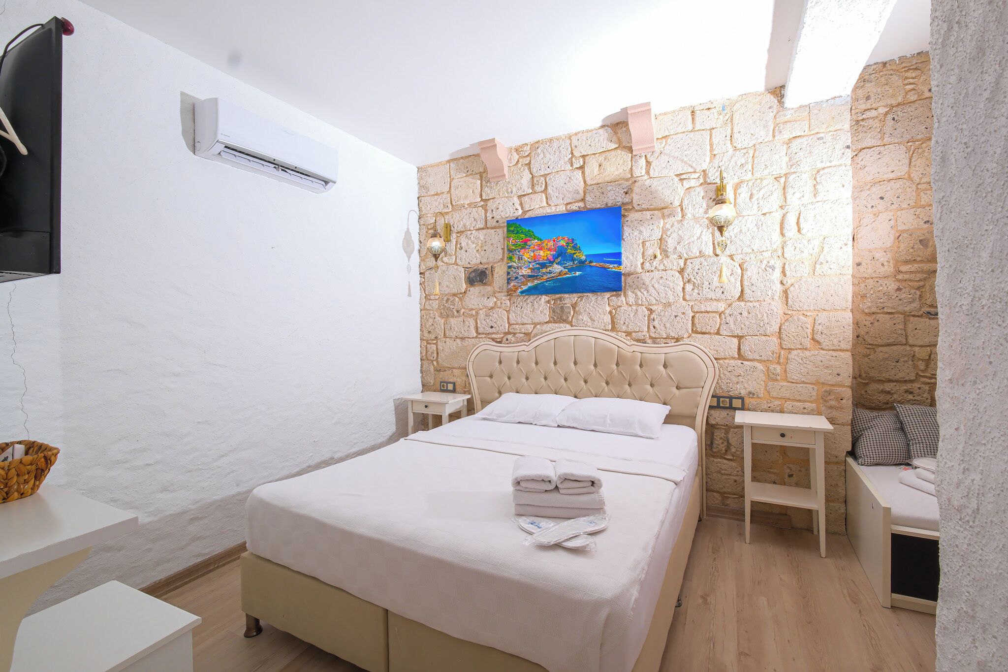 Een slaapkamer met een stenen muur, een bed met witte lakens, een schilderij en een televisie aan de muur.
