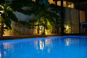 A swimming pool with a tiled edge, surrounded by plants and a stone wall. - Kybele Suites Alacati (Cesme)