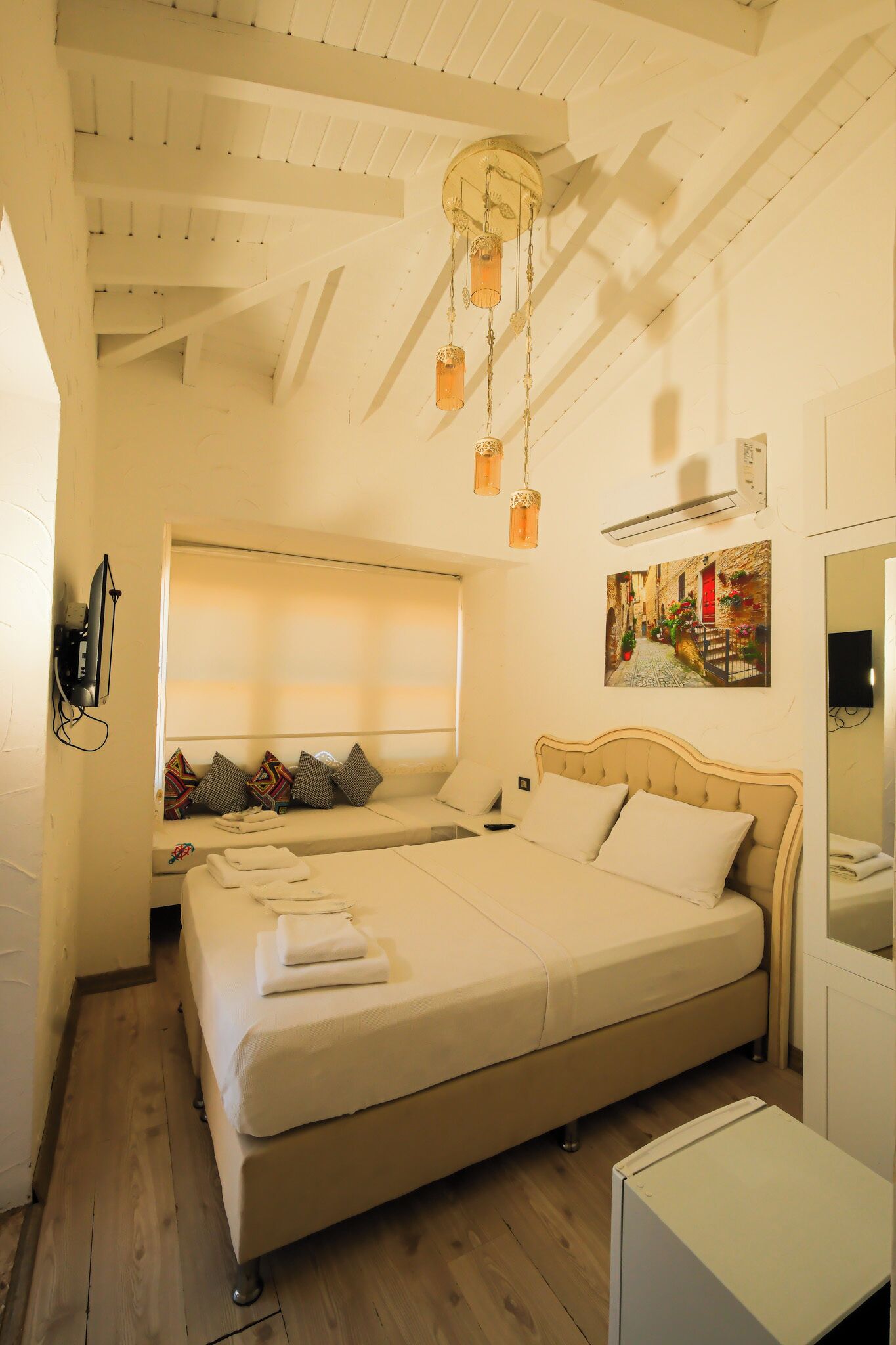 A bedroom with a large bed, a small bedside table, a wall-mounted TV, and a ceiling fan.