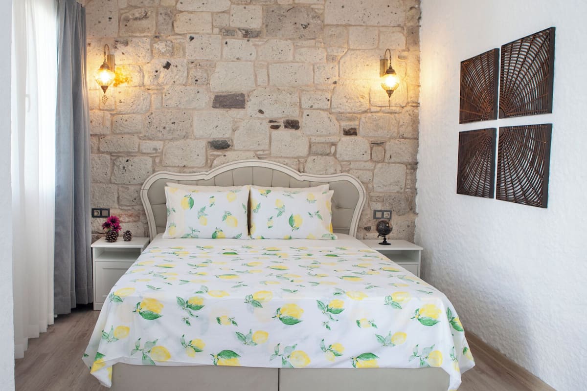 Een slaapkamer met een stenen muur, een bed met een dekbedovertrek met citroenmotief, twee wandlampen en decoratieve muurkunst.