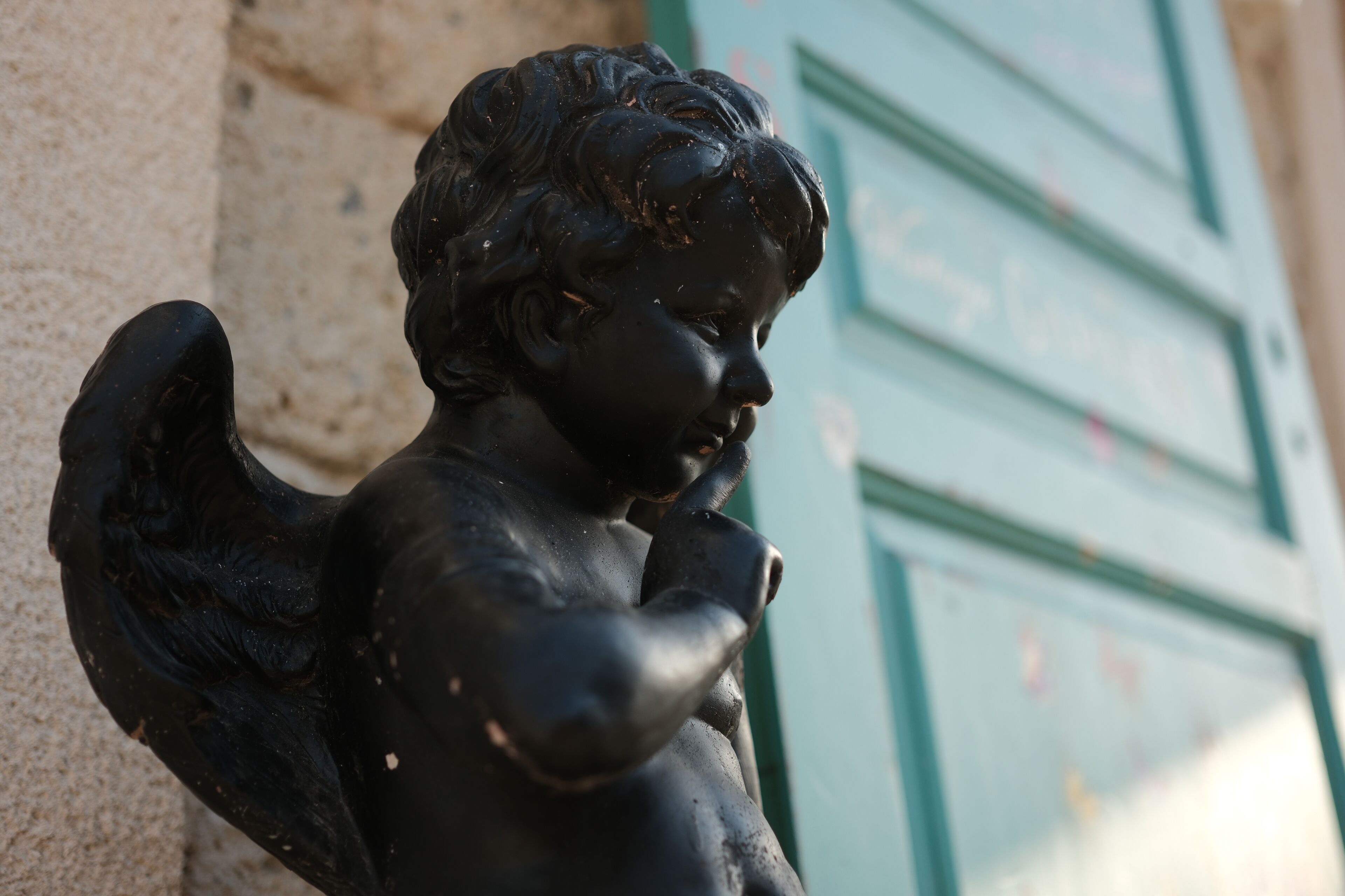 A statue of a child with wings, positioned against a building with green shutters.