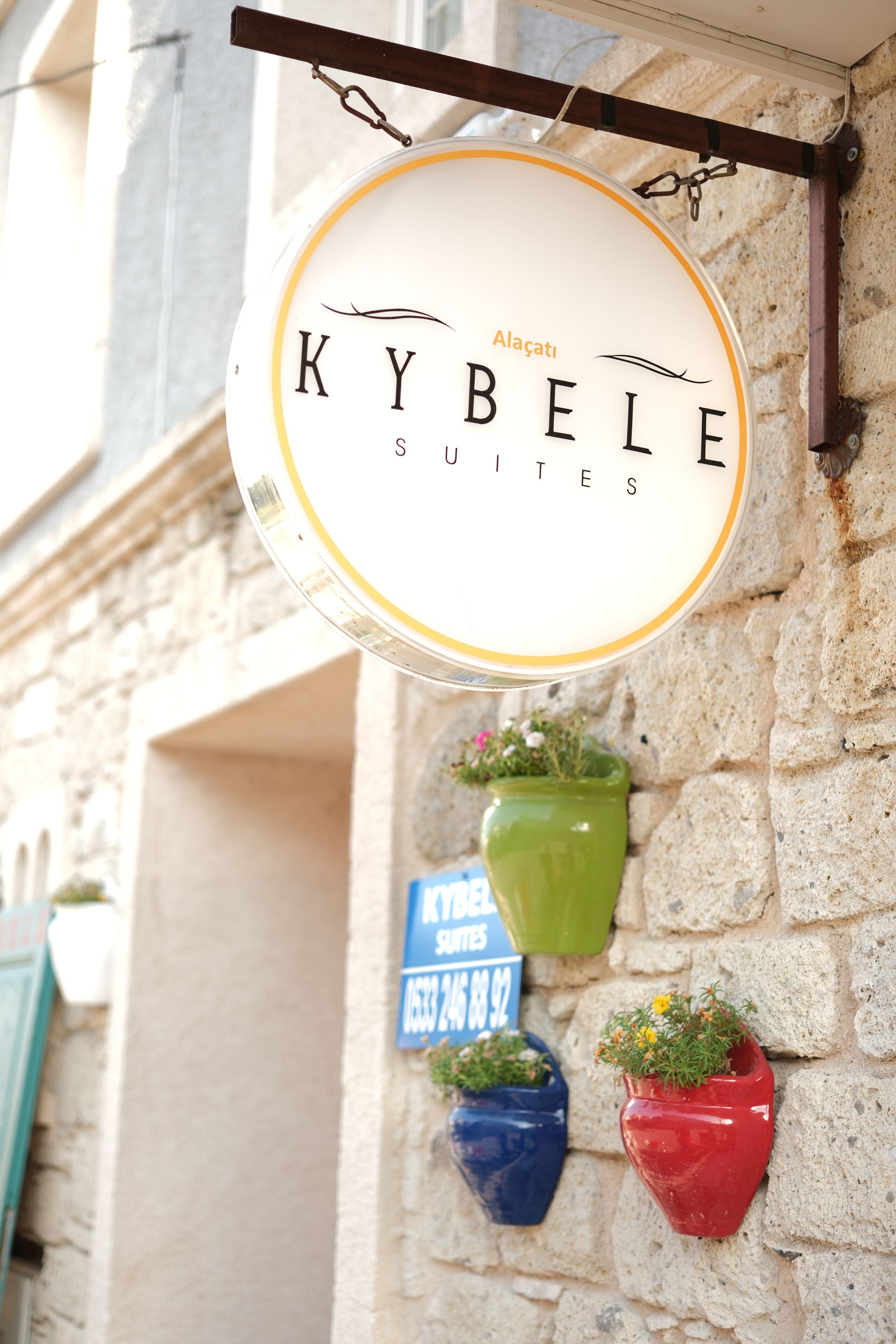 A sign for "KYBELE SUITES" with a hanging sign and three potted plants below.