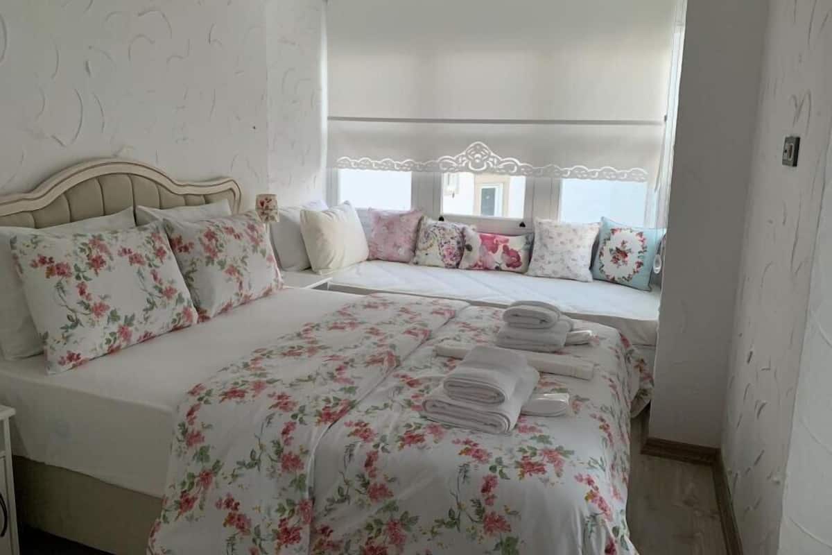 Een slaapkamer met een groot bed, bloemenbeddengoed en een raam met een witte luxaflex.