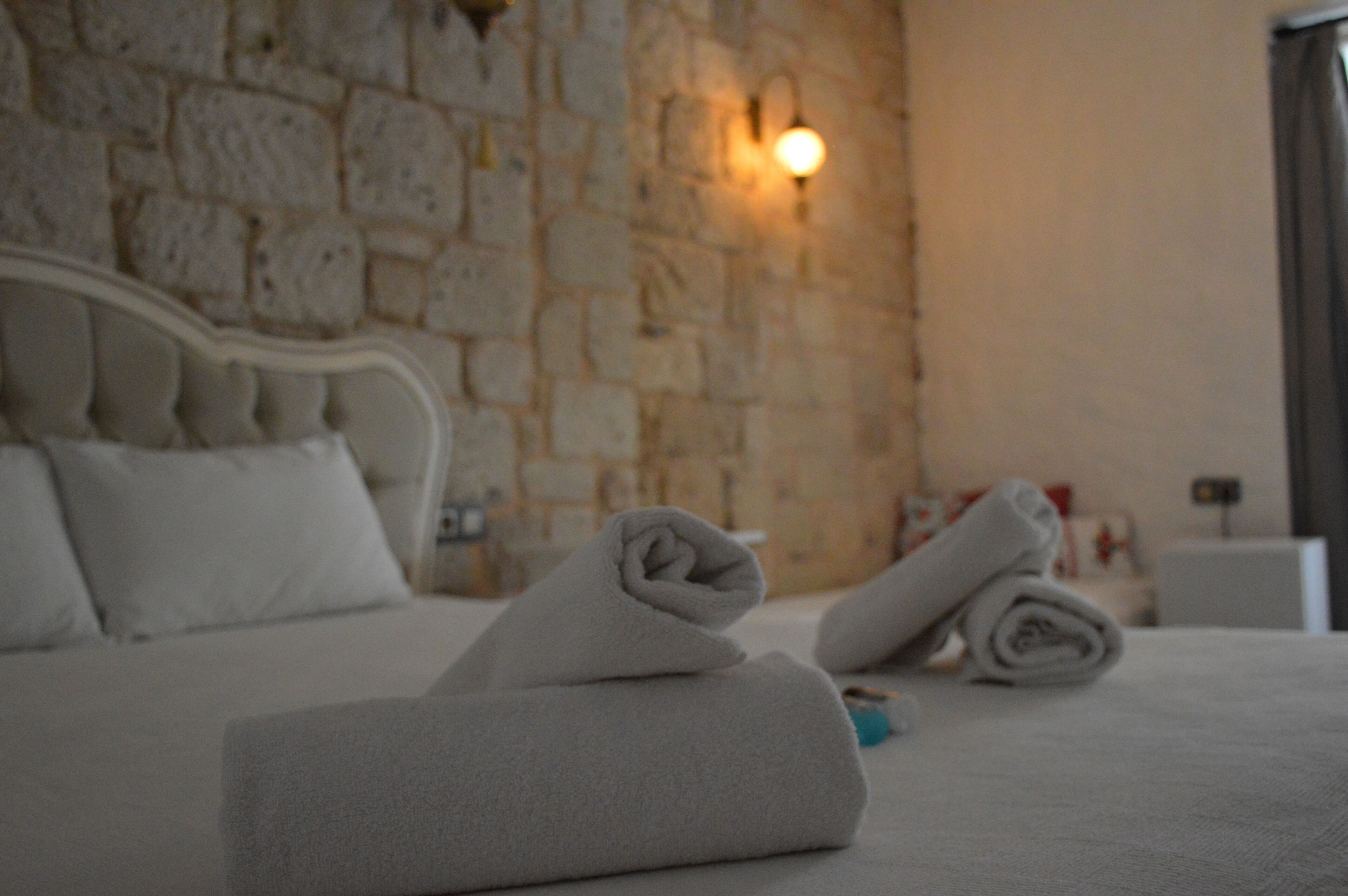 A neatly made bed with rolled towels, a stone wall, and a wall-mounted light fixture.