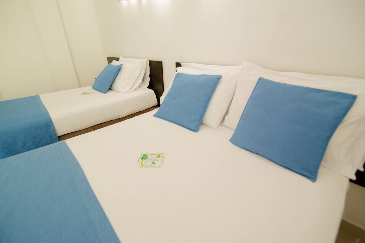 A hotel room with two single beds, each with a blue bedspread and white pillows.