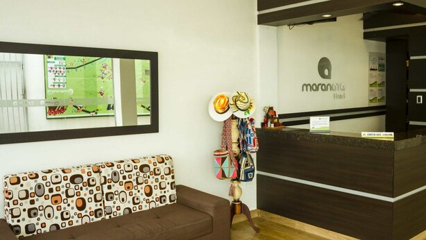 A reception desk with a sign reading "maranato hotel," a patterned sofa, and a wall-mounted mirror reflecting a soccer field. - Hotel Maranatá (Valledupar)