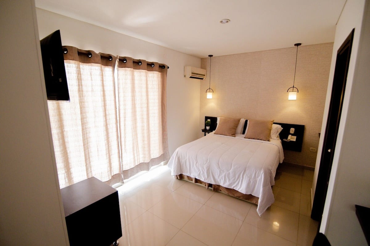 A bedroom with a bed, curtains, an air conditioning unit, and bedside lamps.