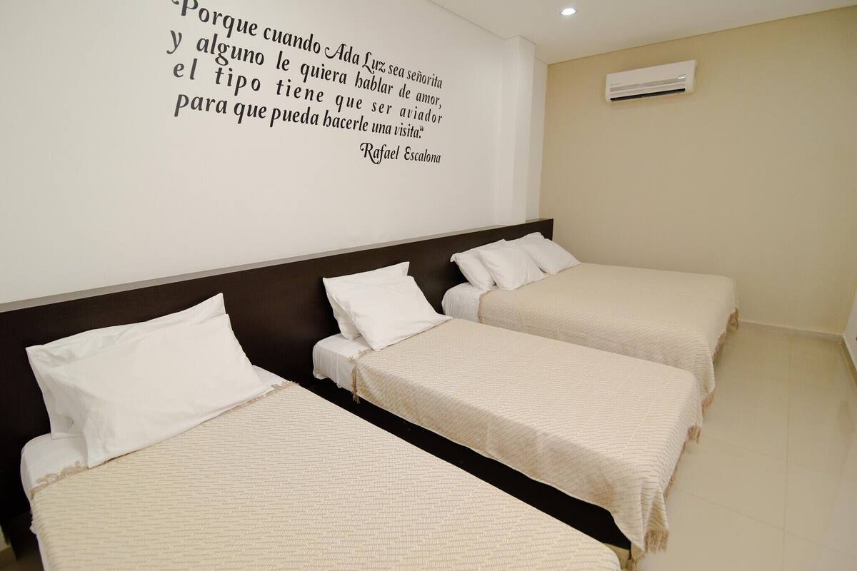 A hotel room with three single beds, a dark headboard, and a wall quote by Rafael Escalona.