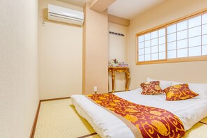 A traditional Japanese-style room with tatami flooring, a bed with a red and gold patterned bedspread, and a window with a grid pattern. - Yado miyabi (Osaka)