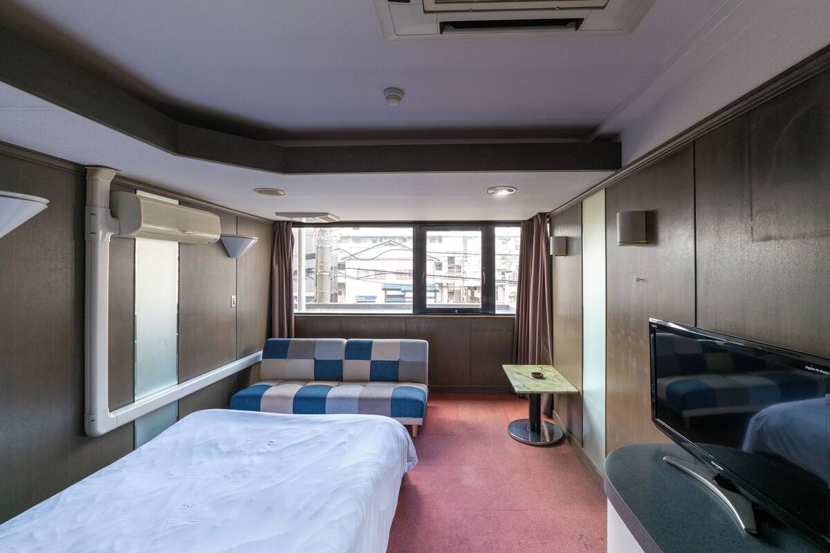A hotel room with a bed, a sofa, a small table, a TV, and a window with curtains.