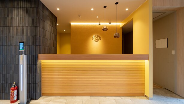 A reception desk with a digital screen, a fire extinguisher, and a wooden counter. - Hotel Sun (Takasaki)
