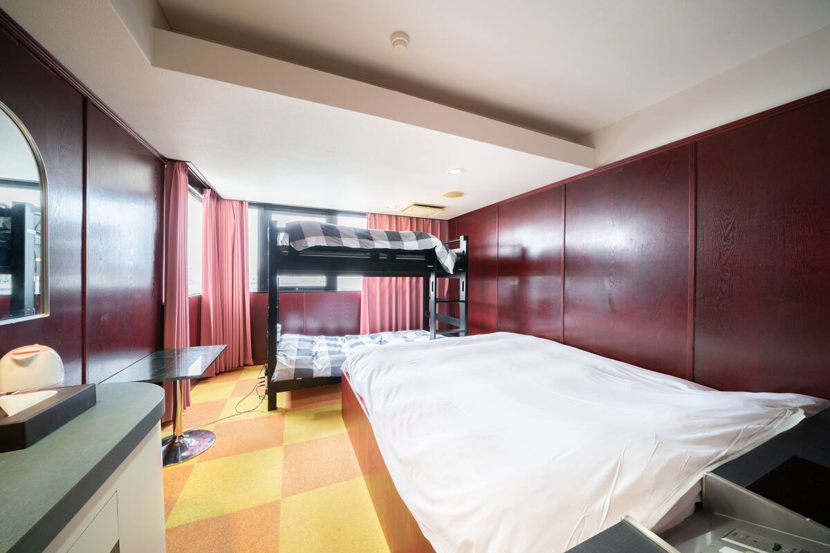 A hotel room with a bunk bed, a desk, a chair, and a window with curtains.