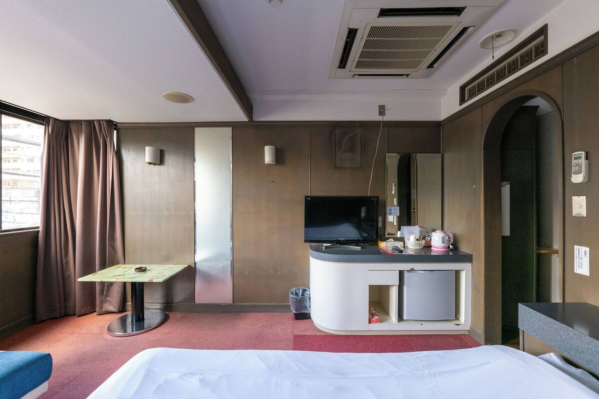 A hotel room with a bed, a desk, a television, a mini-fridge, and a window with curtains.