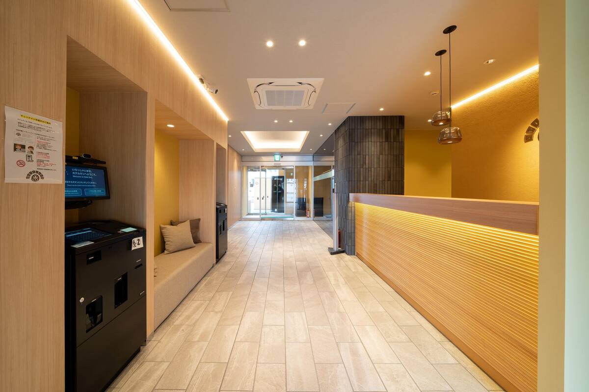 A hotel corridor with a reception desk, a seating area, and a digital information board.