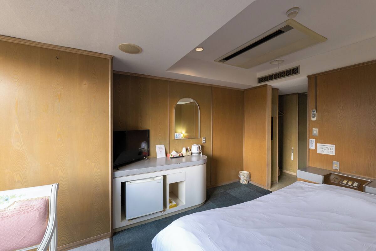 A hotel room with a bed, a desk with a television, a mirror, and a small refrigerator.