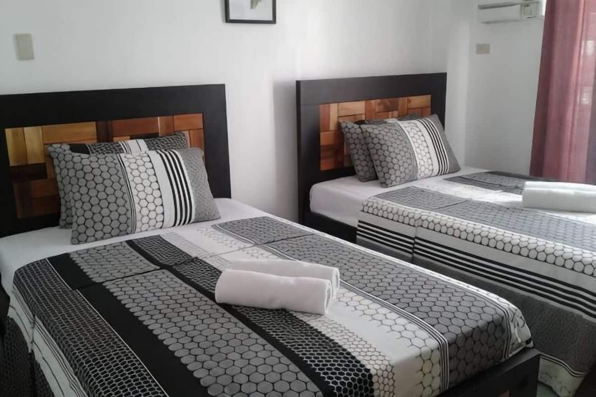 Dos camas con ropa de cama estampada, cabeceras de madera y un cuadro en la pared.