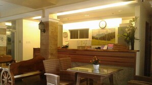 Zona de recepció amb mobiliari de vimet, una taula de recepció de fusta, un rellotge i un quadre de paisatge.