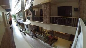Passadís d'hotel de diversos nivells amb una zona central oberta, possiblement un vestíbul o atrium, que presenta una columna de pedra i un balcó amb barana.