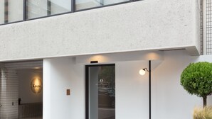 A modern hotel entrance with a glass door, a sign for 'The Hotels Hakata', and a small tree planter on the right. - The Hotels Hakata Kasane Bayside (Fukuoka)