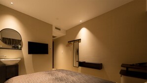 A modern hotel room with a large bed, a bedside table, a built-in TV, a mirror, and a bathroom with a sink and shower. - The Hotels Hakata Kasane Bayside (Fukuoka)