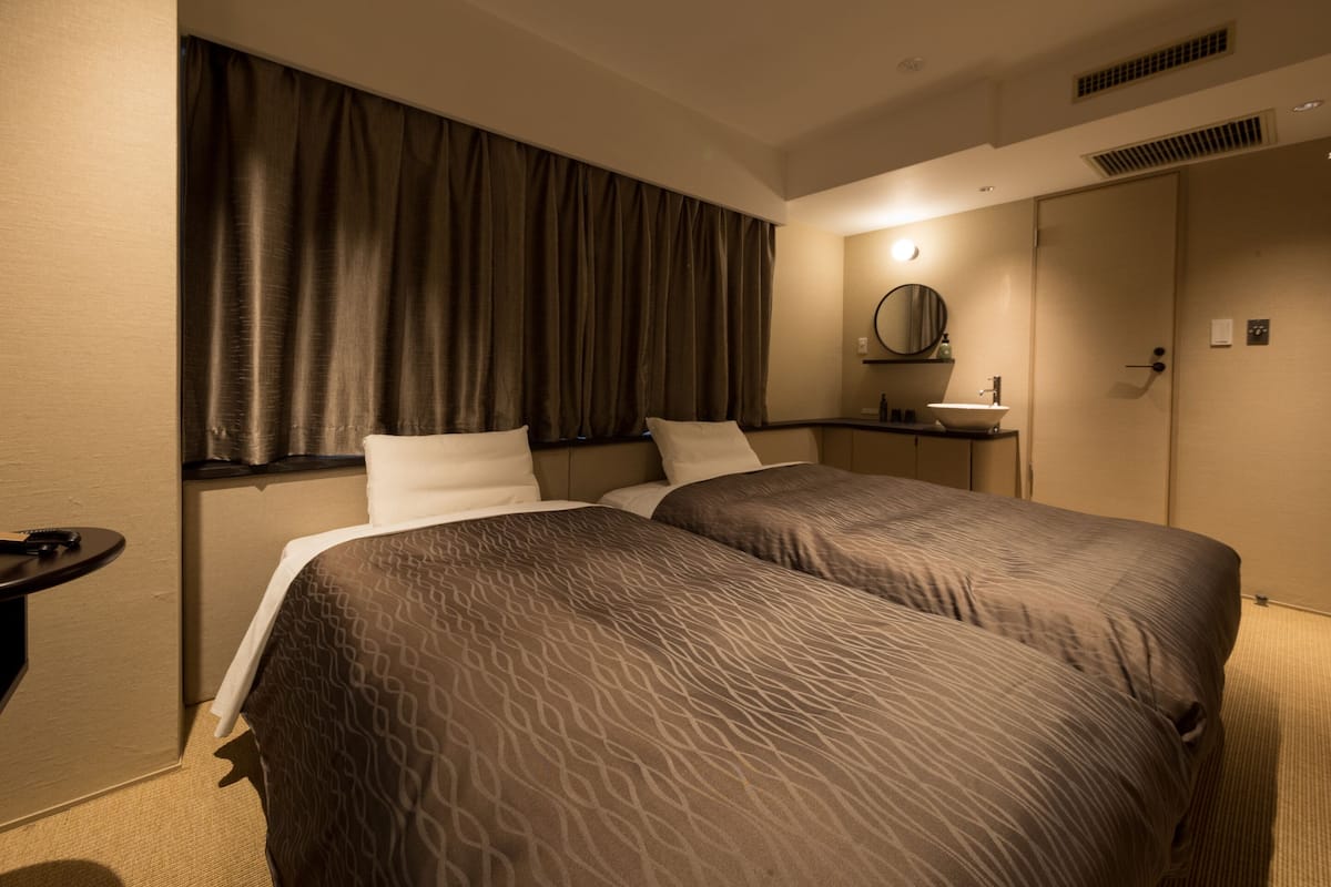 A hotel room with two beds, a bedside table, a mirror, and a bathroom with a sink and toilet.