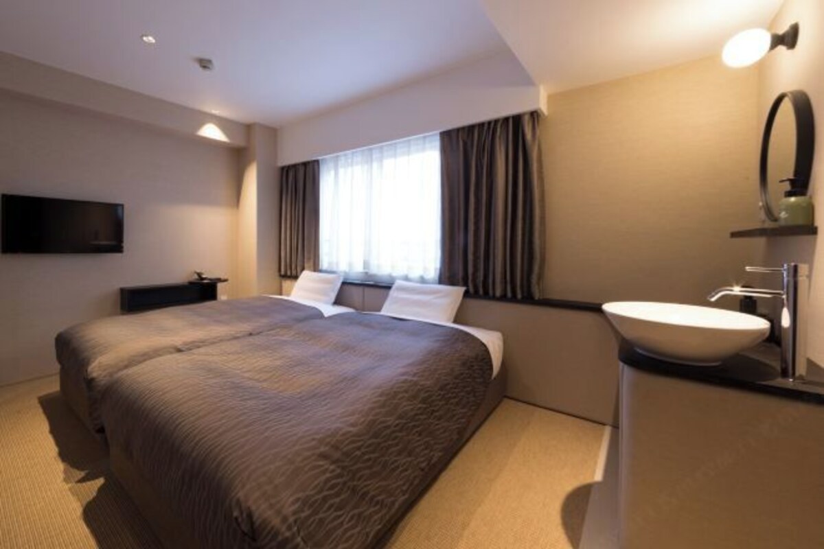 Hotelkamer met een groot bed, nachtkastje, flatscreen-televisie, raam met gordijnen en een badkamer met wastafel en spiegel.