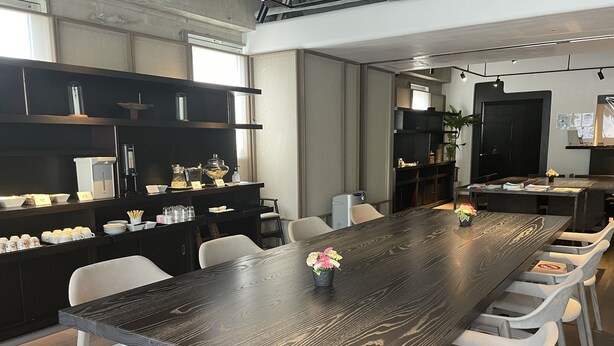 A modern dining area with a long wooden table, white chairs, and a black bar counter with various amenities. - The Hotels Hakata Kasane Bayside (Fukuoka)