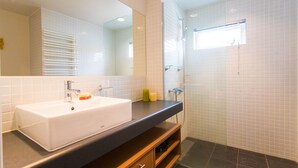 Un baño moderno con un lavamanos blanco, un espejo grande y una cabina de ducha de vidrio.