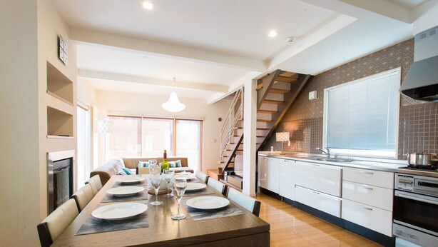 Una cocina moderna con una mesa de comedor de madera para cuatro personas, una escalera y un ventanal con persianas.