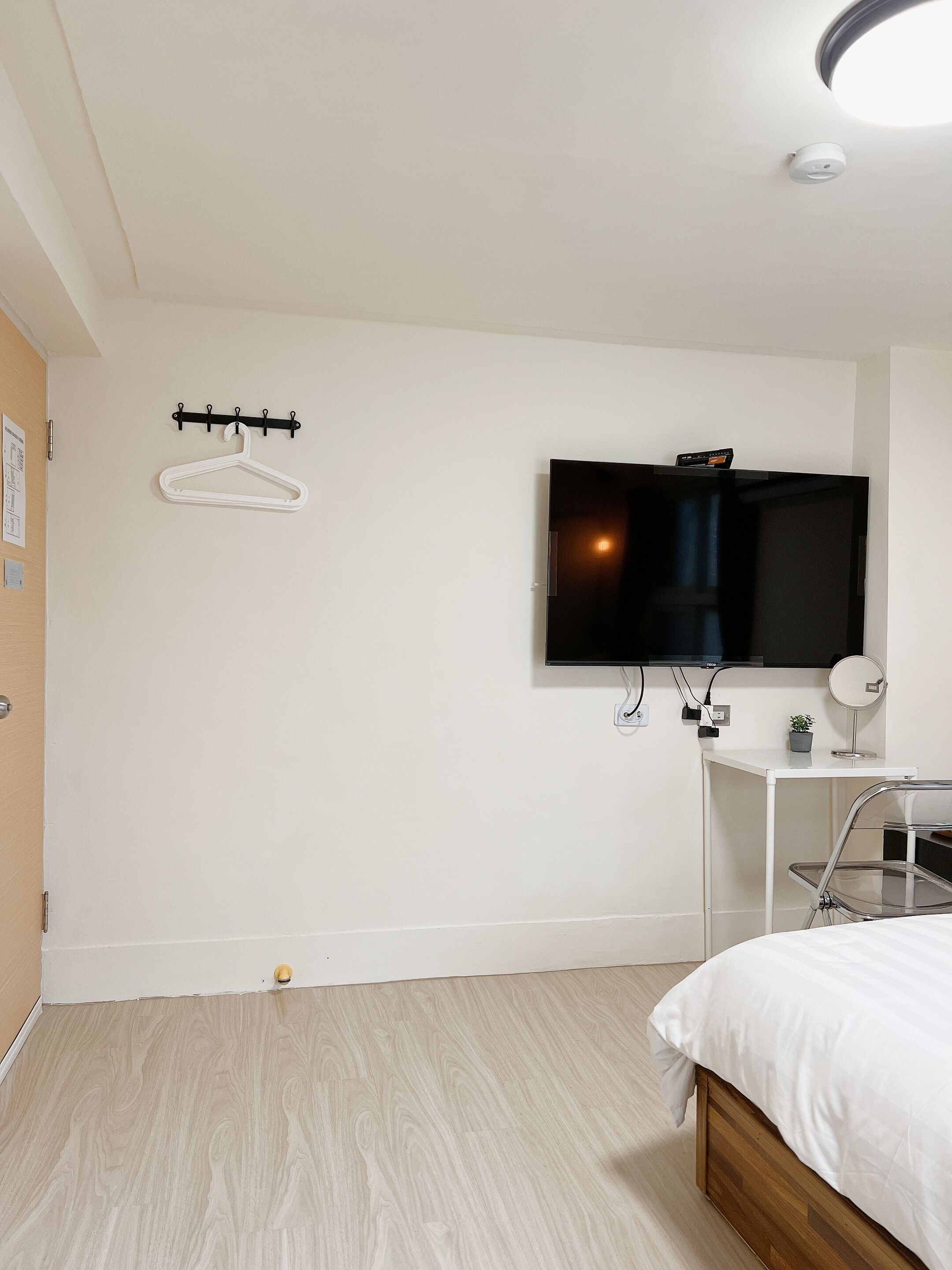 Een hotelkamer met een bed, een aan de muur bevestigde televisie, een klein bureau met een plant en een kapstok.