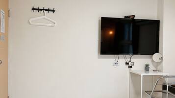 Een hotelkamer met een bed, een aan de muur bevestigde televisie, een klein bureau met een plant en een kapstok.