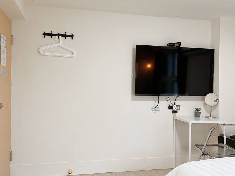 Een hotelkamer met een bed, een aan de muur bevestigde televisie, een klein bureau met een plant en een kapstok.