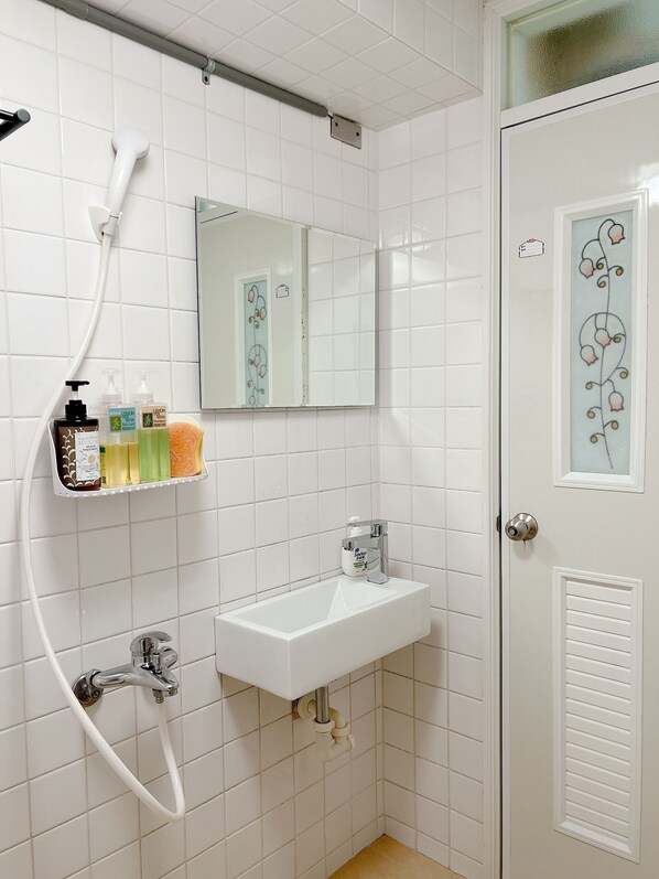 A bathroom with a white sink, a mirror, a shower, and toiletries on a shelf. - Relax Inn (Tainan)