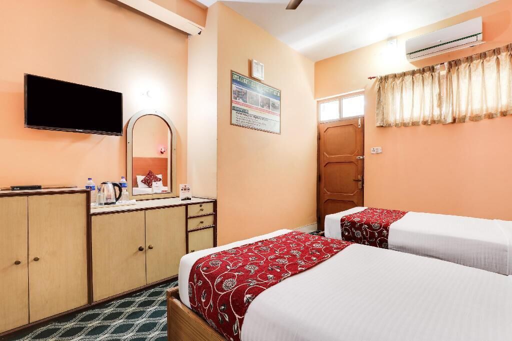 A hotel room with two beds, a TV, a mirror, a desk with a kettle, and a poster on the wall.