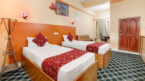 A hotel room with two beds, a wooden headboard, a small desk, and a wardrobe.